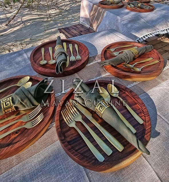 Mesa elegante Zizal Mayan Cuisine · cubiertos dorados y vajilla artesanal en palapa frente al mar de Sisal